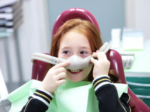Smiling young girl in dental chair wearing a nitrous oxide sedation nose mask