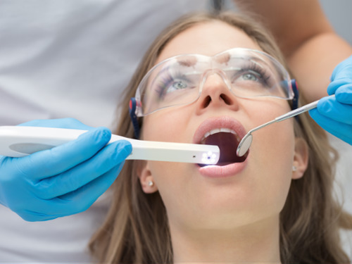Dentist using an intraoral camera to examine a female patient's teeth during a dental exam