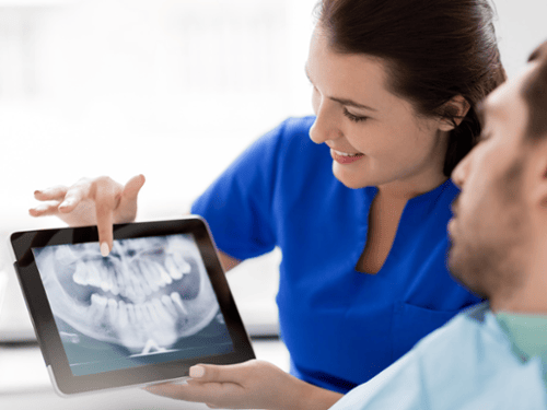 Dental hygienist reviewing digital X-ray images on a tablet with a patient